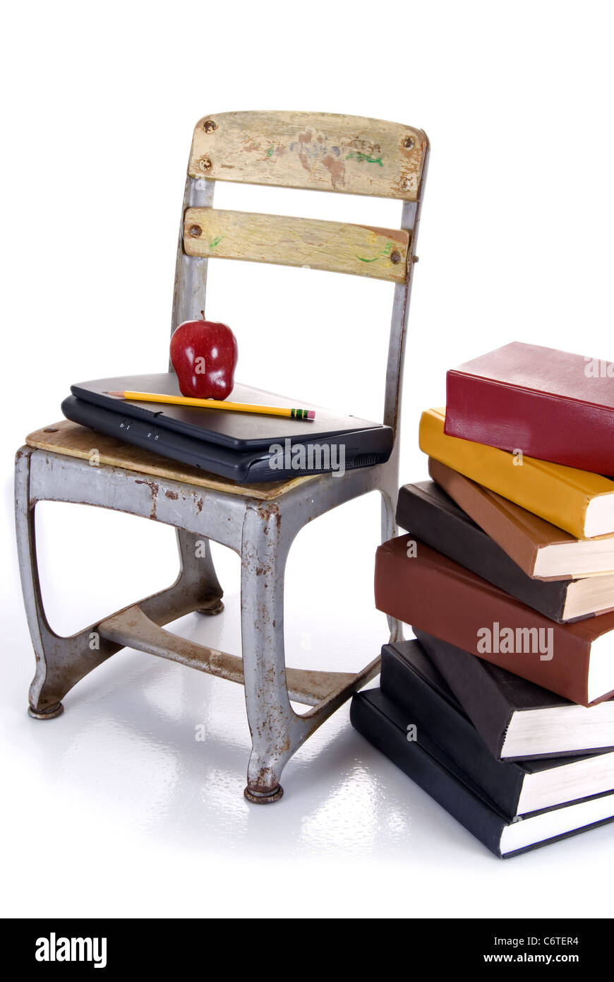 Apretar Tanga estrecha comentarista Un vintage silla escolar del niño sosteniendo un portátil con una manzana y  lápiz encima de ellos. Al lado de la silla es una pila de libros Fotografía  de stock - Alamy