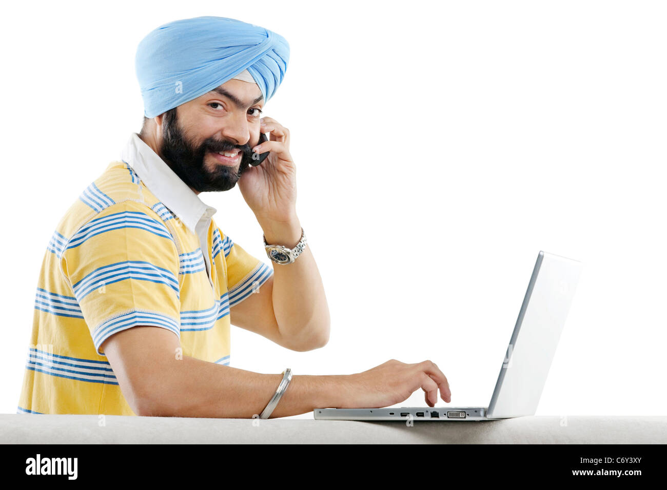 Hombre Sikh hablar por teléfono mientras se trabaja en un portátil. Foto de stock