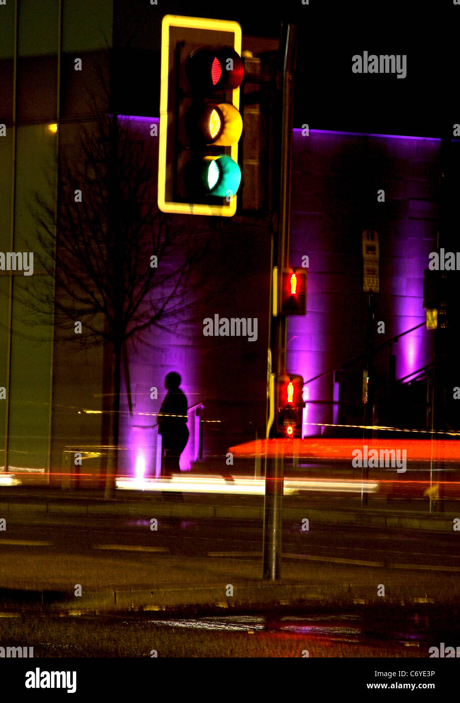 Un paso de peatones en la noche en el centro de la ciudad con estelas de luz desde el paso de los vehículos y la silueta de una persona Foto de stock