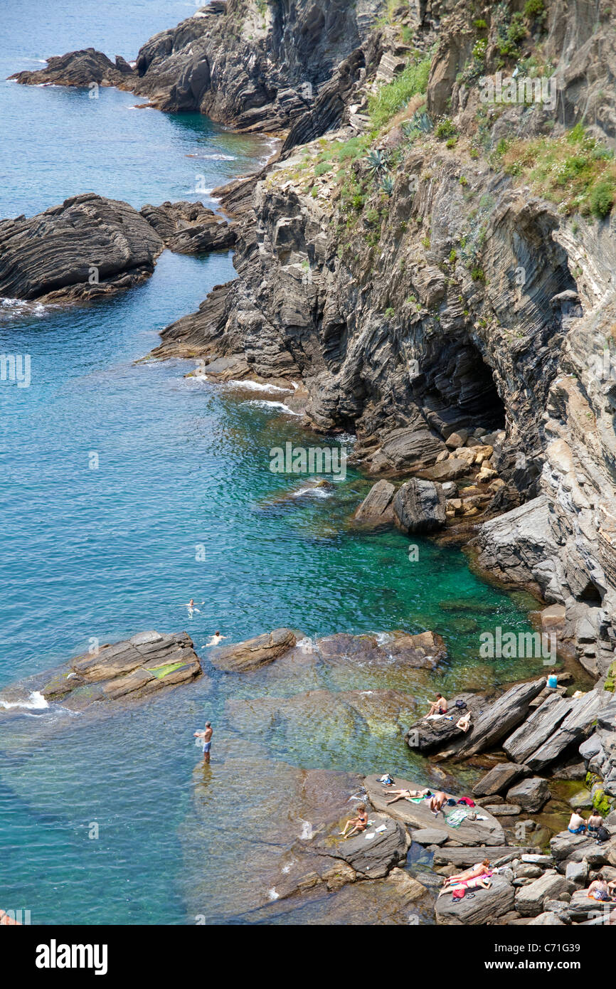 La gente en la playa rocosa, Vernazza, el parque nacional de Cinque Terre, sitio del Patrimonio Mundial de la Unesco, en Liguria, Italia di Levante, el mar Mediterráneo, Europa Foto de stock