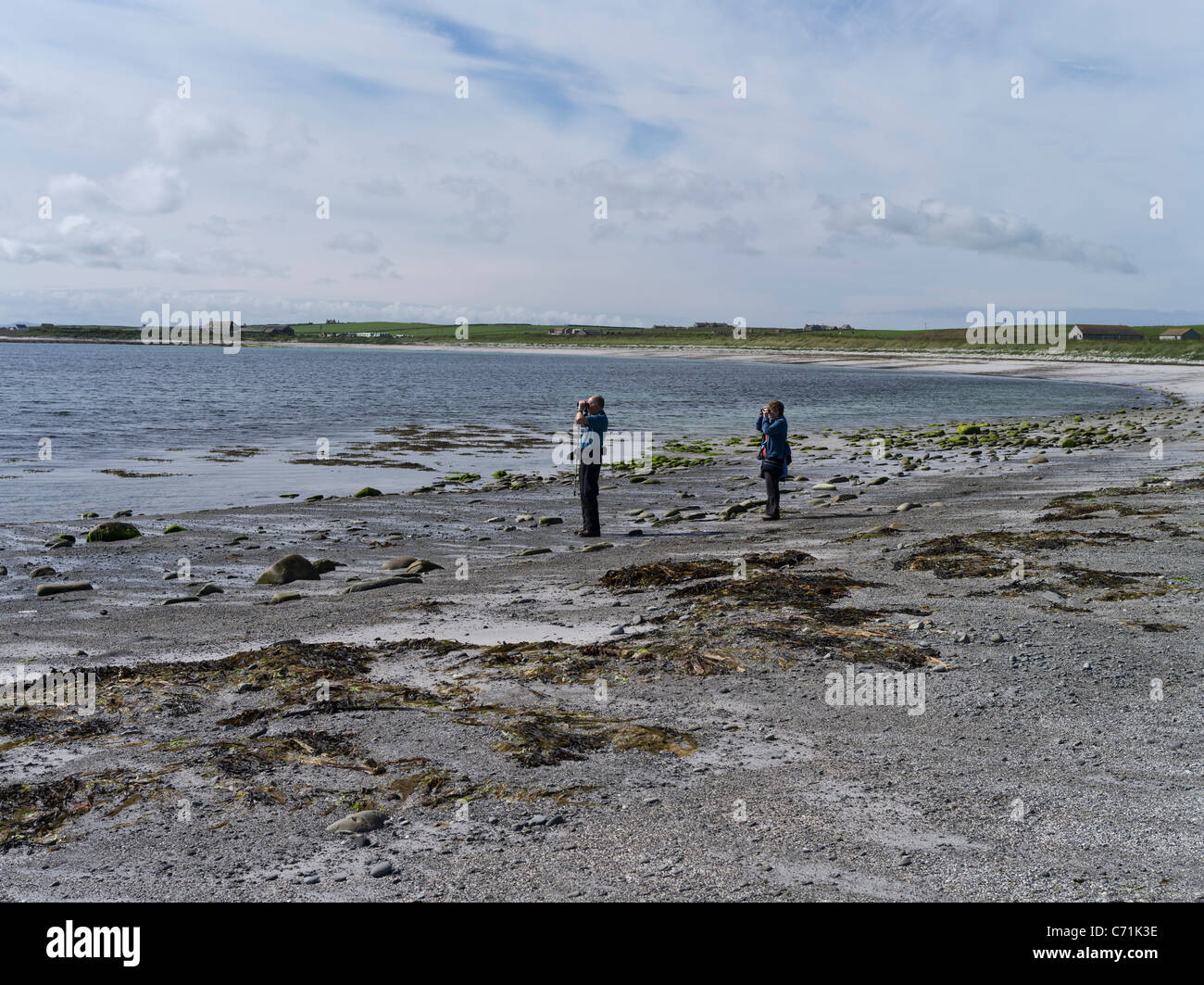 dh PAPA WESTRAY ORKNEY dos observadores de aves observando con binoculares a la orilla del mar observadores de aves de playa escocia observadores de costa islas observación de aves gente Foto de stock