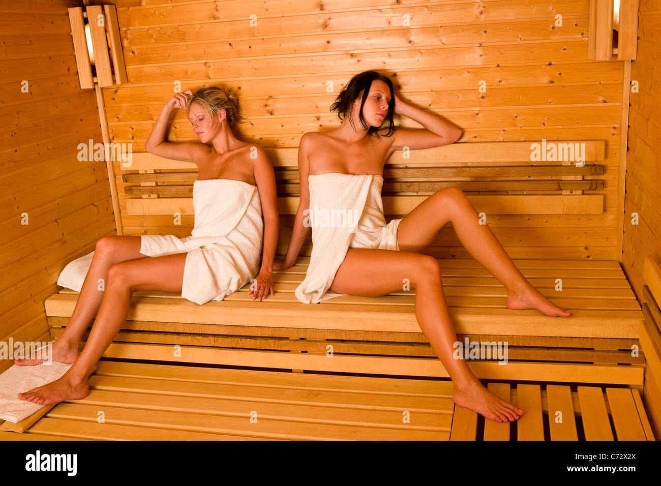 Dos hermosas mujeres saludables sauna relajante sentarse envuelto en toalla Foto de stock