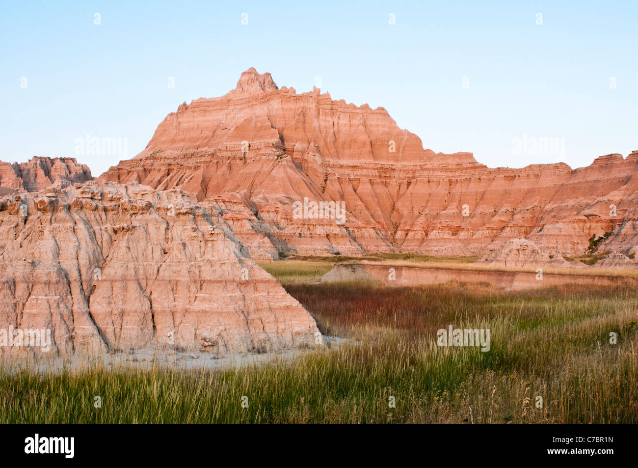 Luz del atardecer brilla en capiteles esculpidos que se elevan por encima de praderas en el Parque Nacional Badlands. Foto de stock