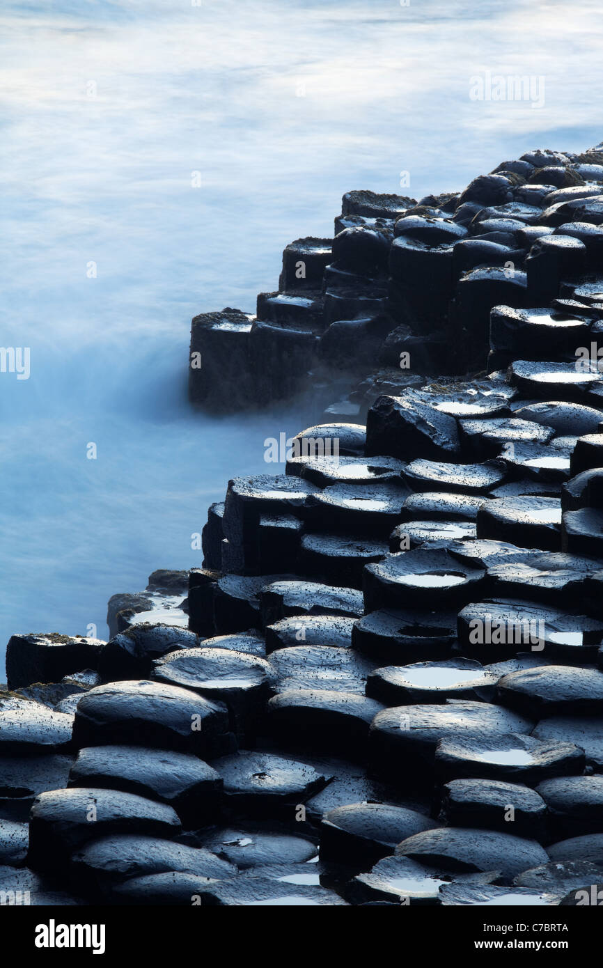 Olas salpicando sobre columnas de basalto cerca del atardecer, Giant's Causeway, Condado de Antrim, Irlanda del Norte, Reino Unido Foto de stock