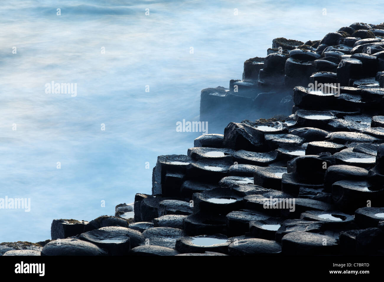 Olas salpicando sobre columnas de basalto cerca del atardecer, Giant's Causeway, Condado de Antrim, Irlanda del Norte, Reino Unido Foto de stock