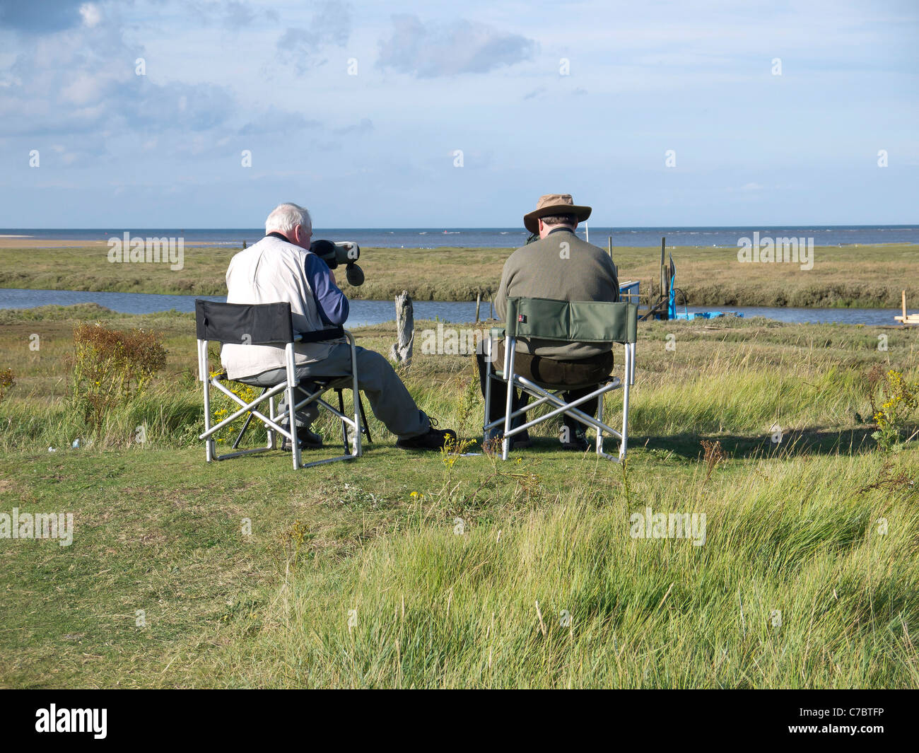 Dos hombres sentados en sillas de campamento de observación de aves en la desembocadura del arroyo Thornham parte de la Reserva Natural de Holme Norfolk Foto de stock