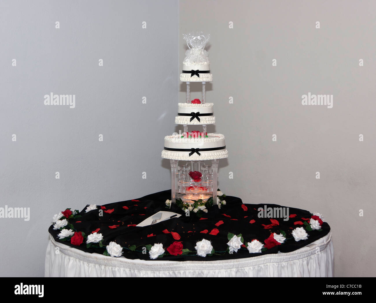 Pastel de boda multicapa con fuente de agua y topper sobre una mesa  decorada con tela negra roja y pétalos de rosas blancas Fotografía de stock  - Alamy