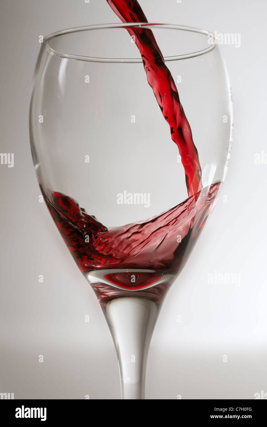 El vino tinto que se vierte en una copa de vino limpio contra un gris de procedencia. Foto de stock
