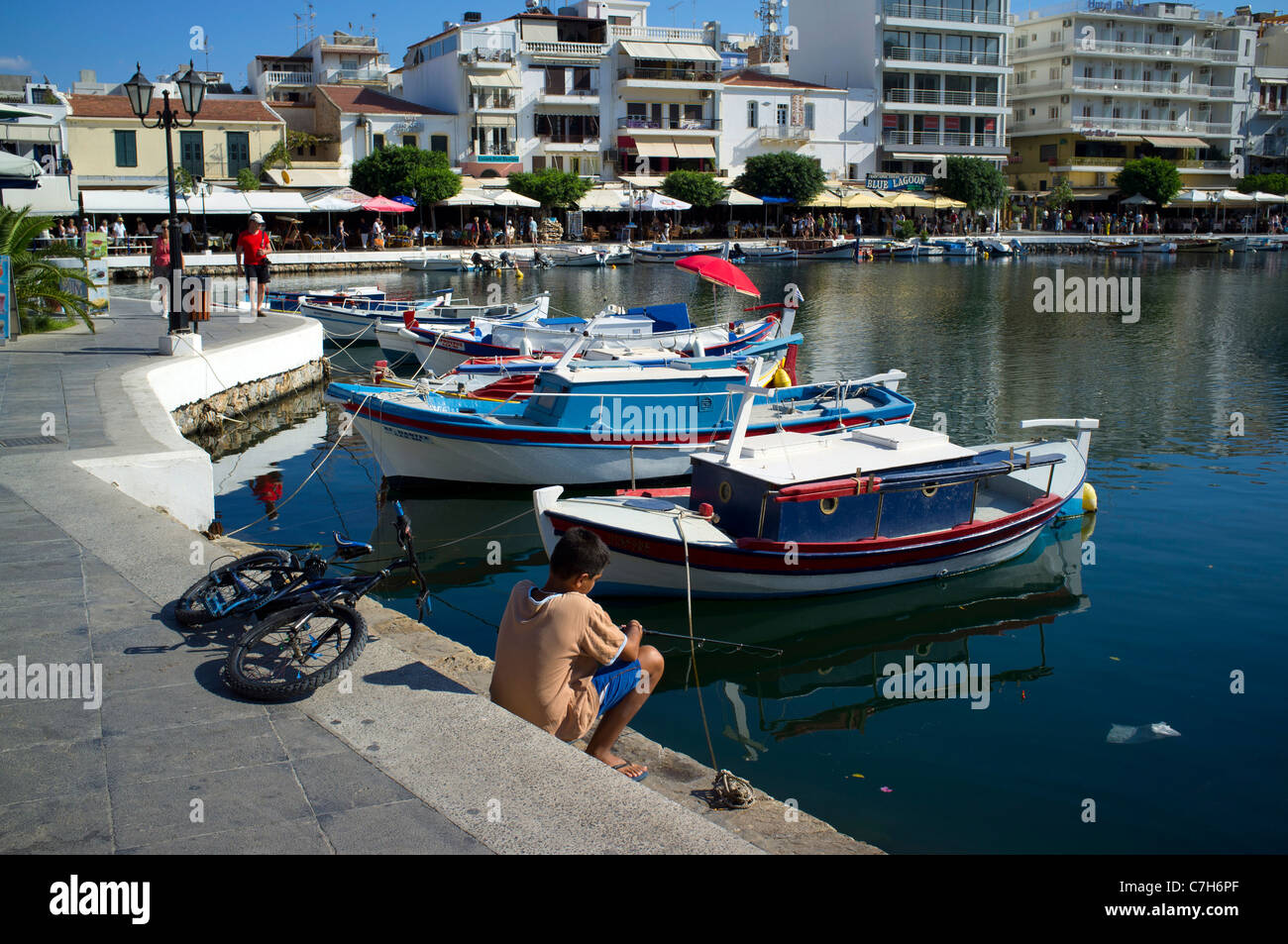 Boy bicicleta Pesca Lago Voulismeni Creta Grecia puerto Boat Harbor restaurantes vacaciones destino soleado de verano Sol bicicleta Foto de stock