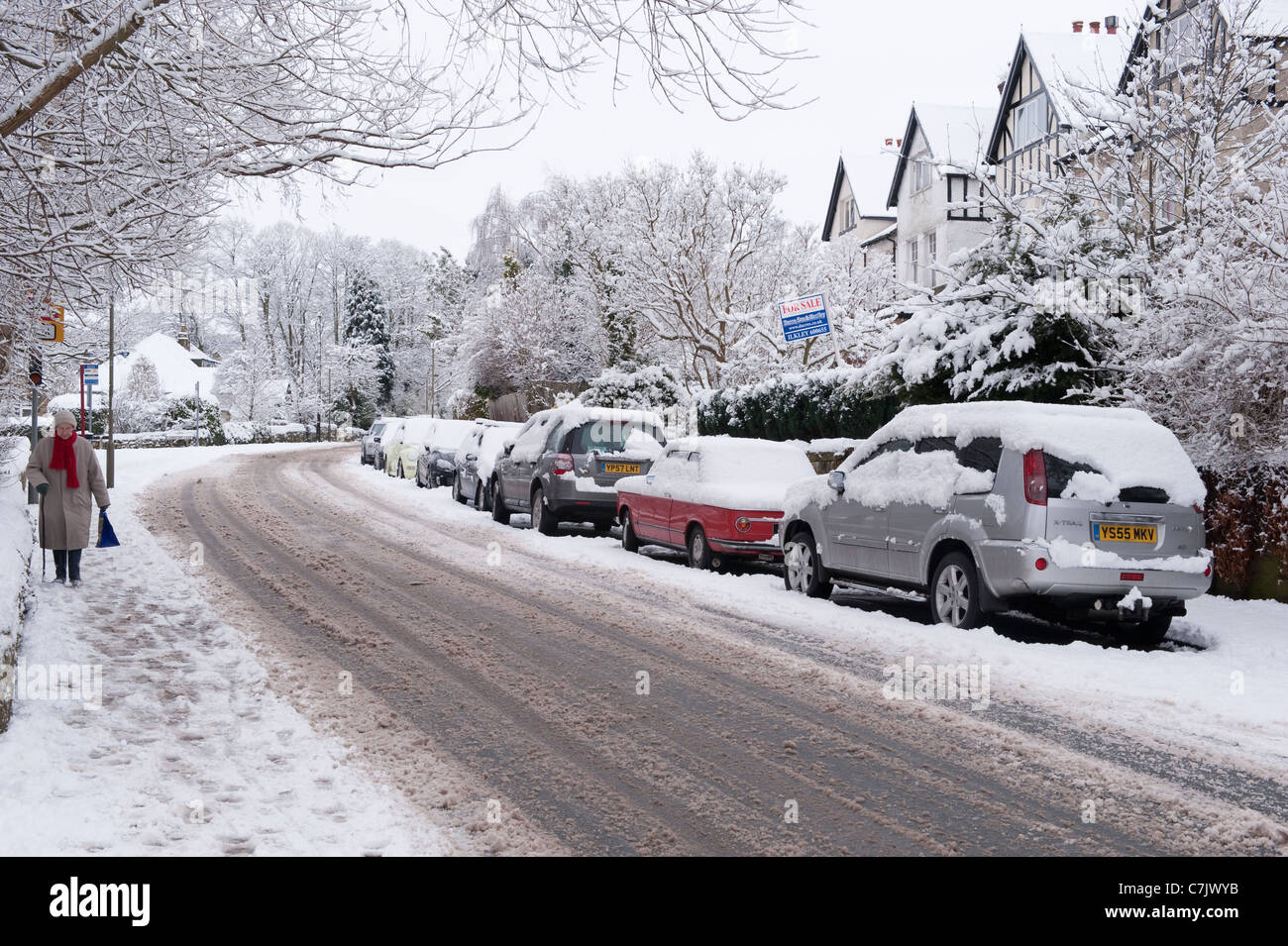Winter Village Street (pistas sobre carreteras cubiertas de nieve, coches estacionados, paseos peatonales, huellas en el pavimento) - Burley en Wharfedale, Inglaterra, GB, Reino Unido. Foto de stock