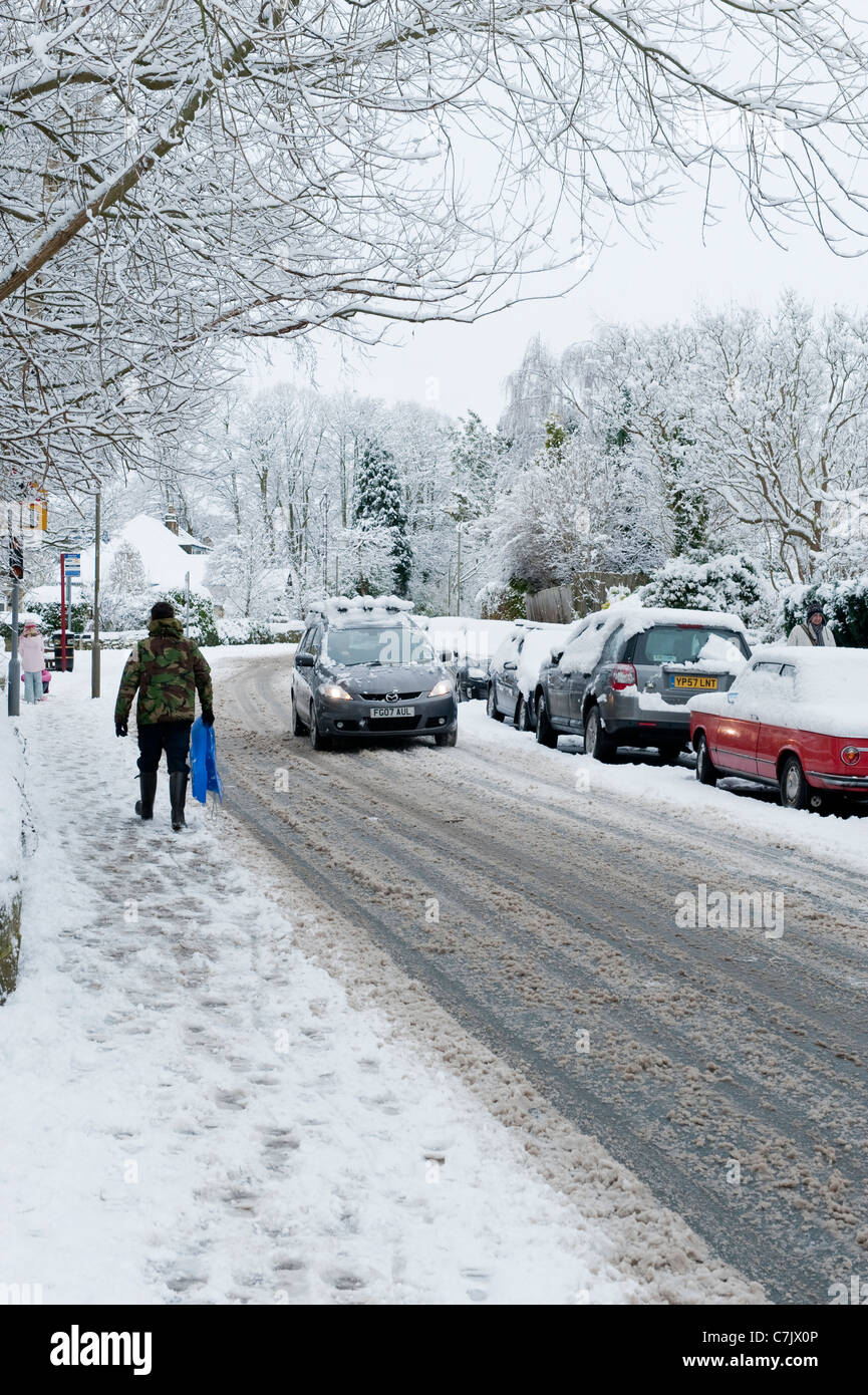 Calle del pueblo de invierno (condiciones de conducción nevadas, coches en carretera, peatones caminando, pavimento cubierto de nieve) - Burley en Wharfedale, Inglaterra, GB, Reino Unido. Foto de stock