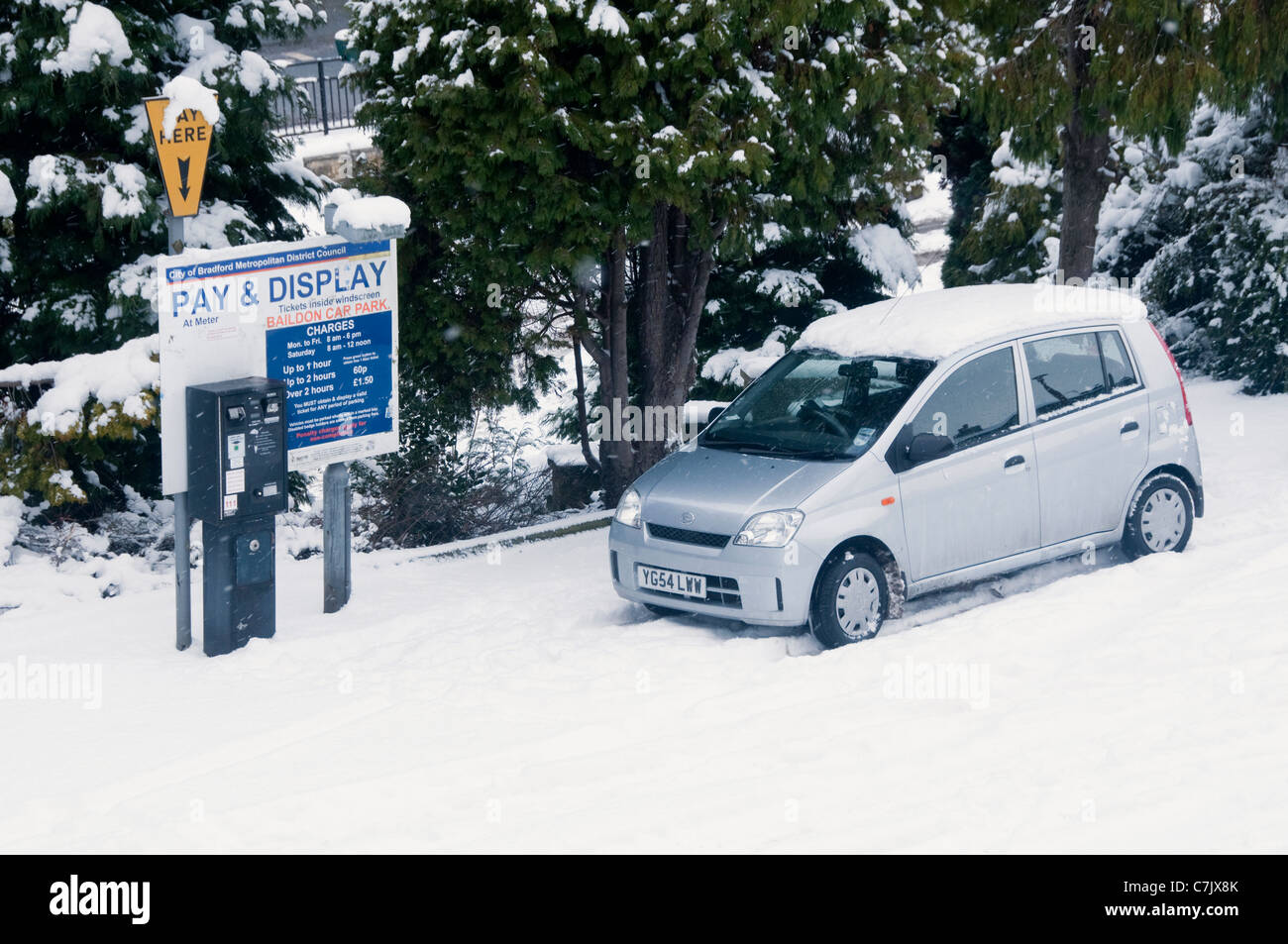 Aparcamiento cubierto de nieve de invierno (coche de plata estacionado en la nieve por pagar y la máquina de venta de entradas, lista de cargos en el cartel) - Baildon, West Yorkshire, Inglaterra, Reino Unido. Foto de stock