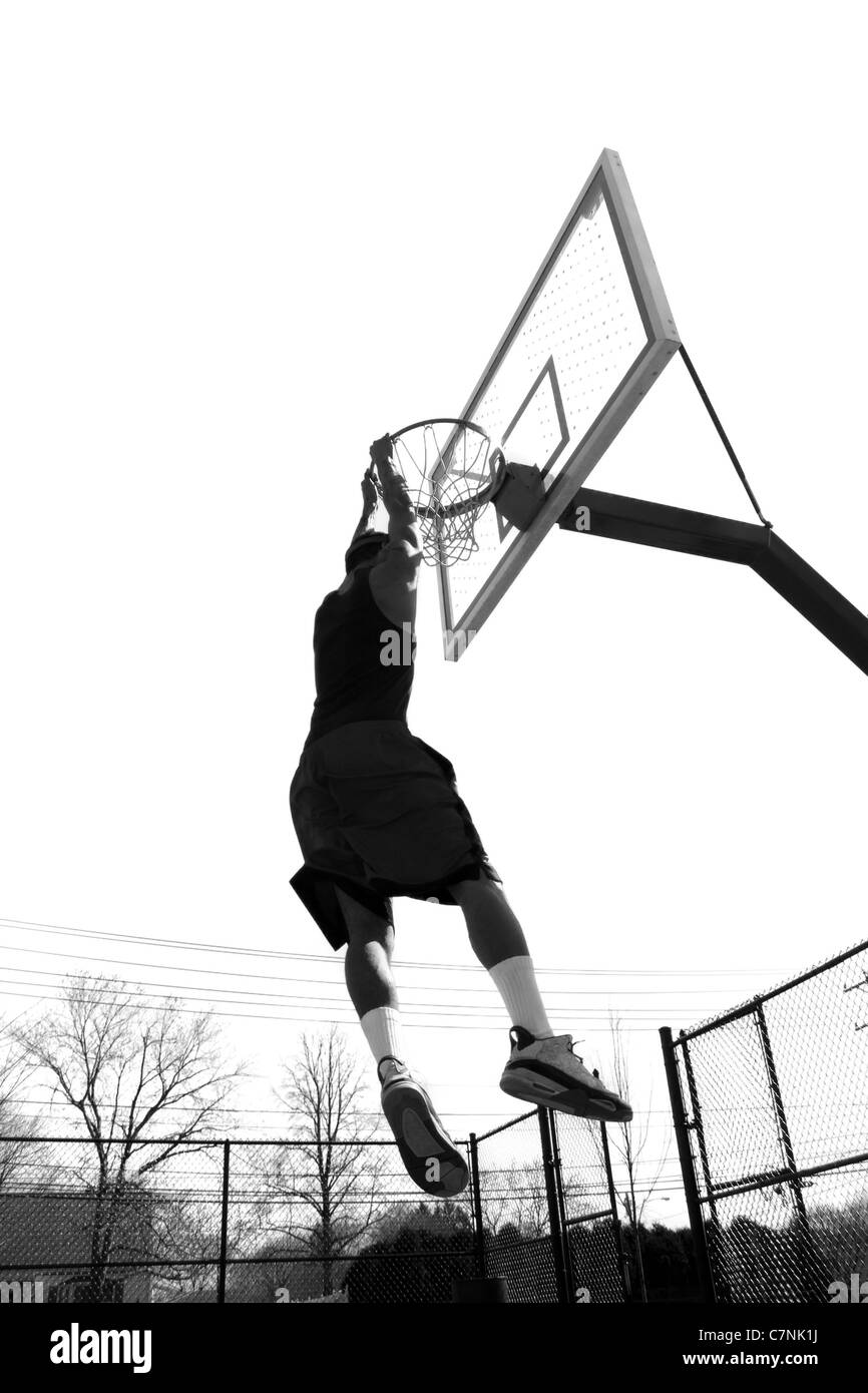 Un jugador de baloncesto que cuelgan de la llanta después slam mojando la bola en blanco y negro. Foto de stock