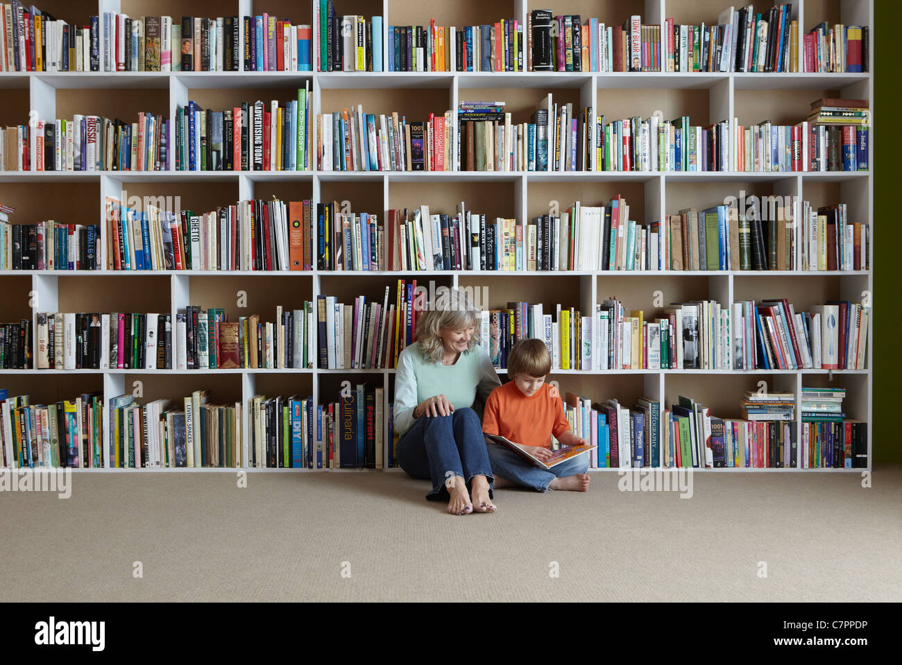 Mujer leyendo con su nieto por estantería Foto de stock