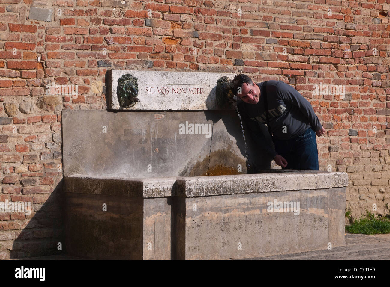 Un joven hombre adulto plantea antes de beber de la fuente de la comunidad junto al edificio público de Città della Pieve, Italia. Foto de stock