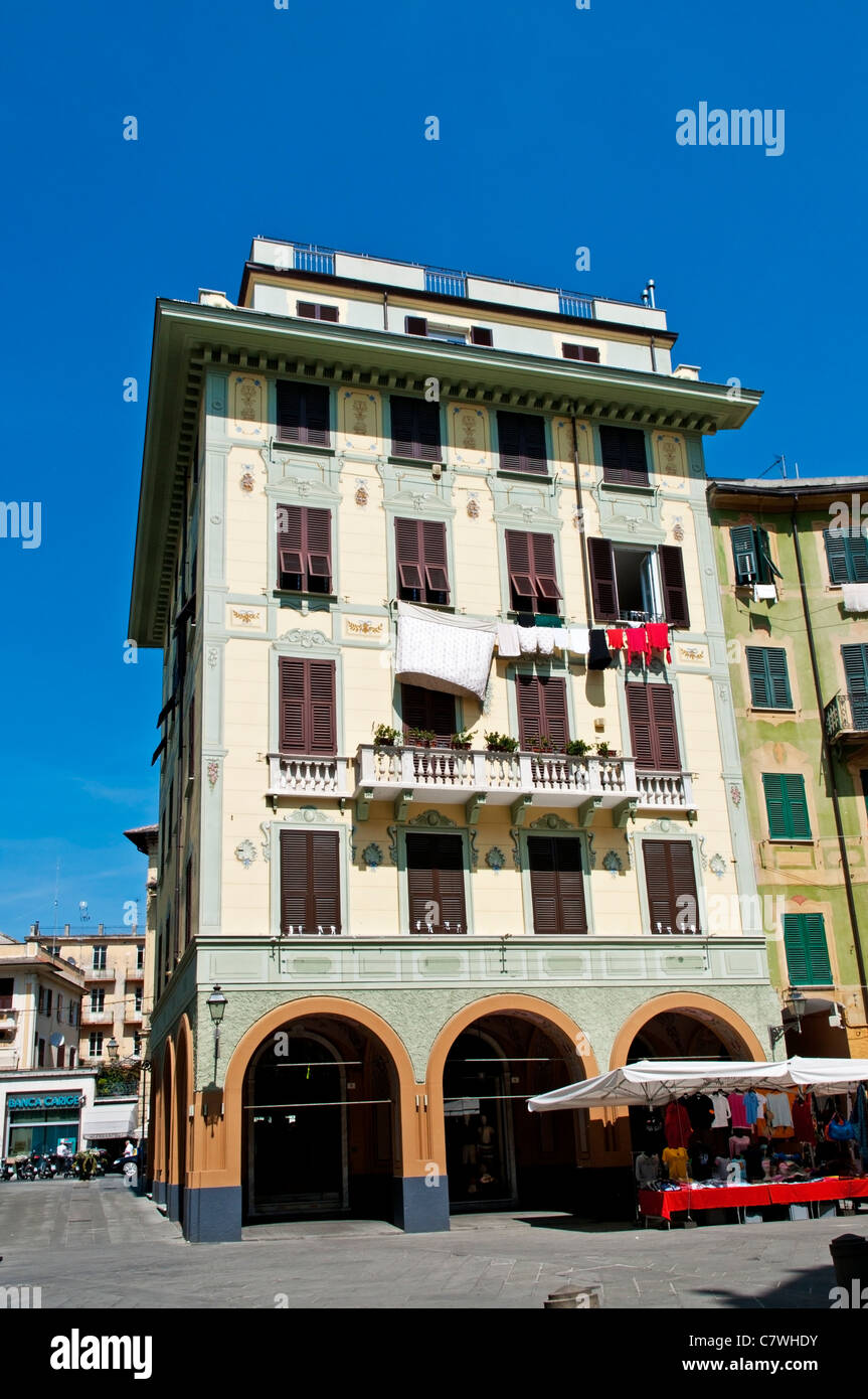 Un bloque de apartamentos pintado en colores pastel por encima de una fila de tiendas en la plaza sombreada de Caprera, Santa Margherita Ligure, Italia Foto de stock