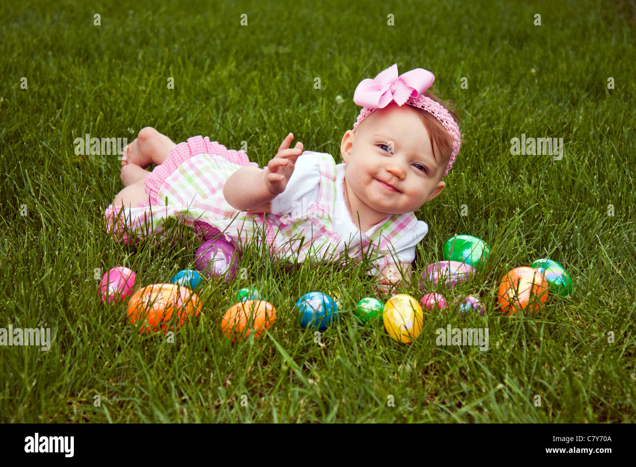 Hermoso bebé tendido en la hierba con un surtido de huevos de Pascua de colores Foto de stock