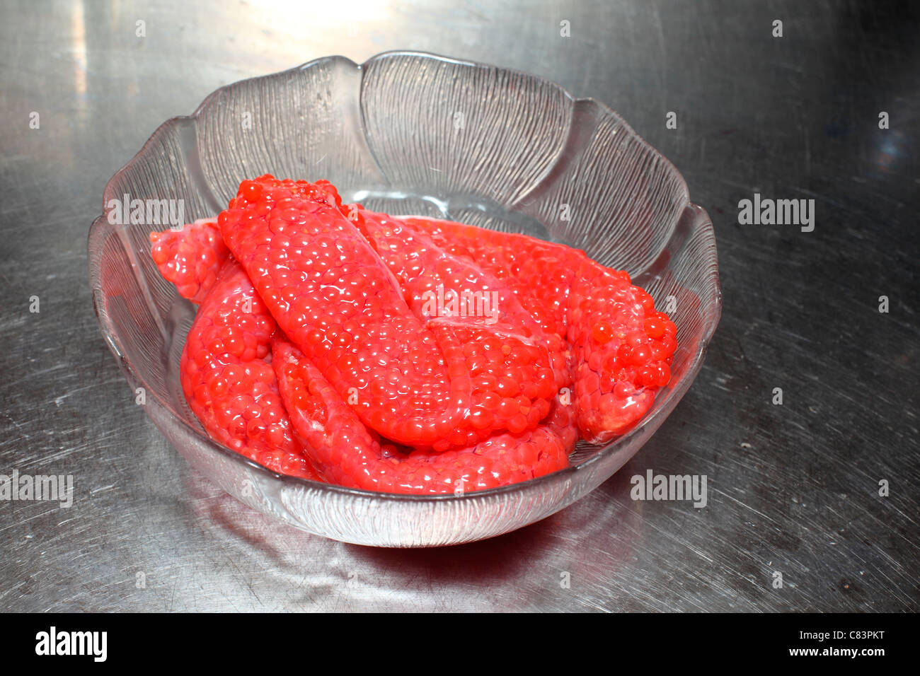 Huevas de salmón en un tazón de vidrio en un contador de acero inoxidable Foto de stock