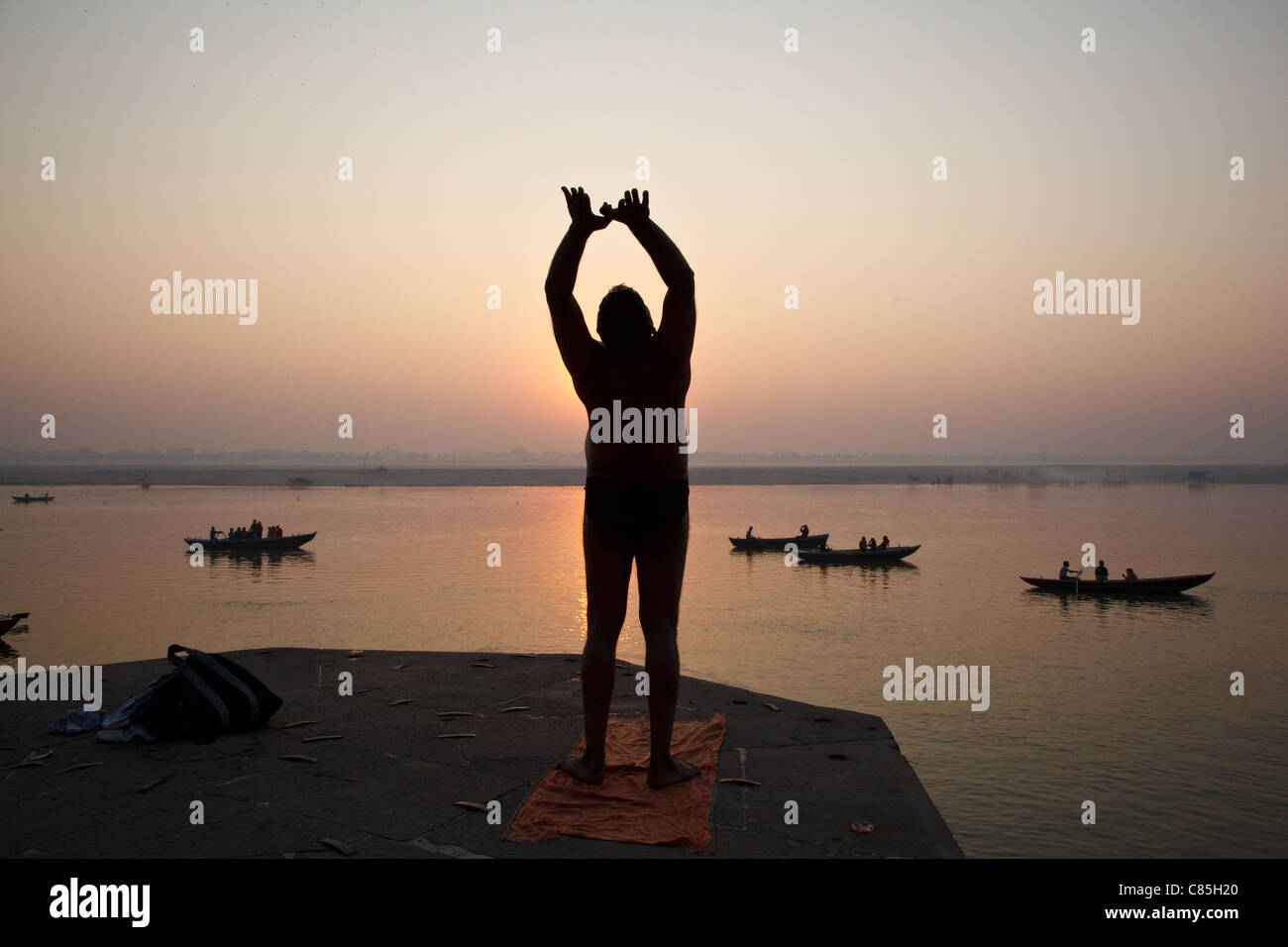 Un hombre ejerce sobre el río Ganges a la puesta de sol en Varanasi, India Foto de stock
