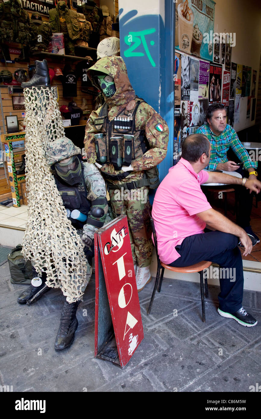 Tienda de venta de ropa militar y junto a un café donde los hombres  sentados hablando juntos en el mercadillo de Monastiraki, en Atenas, Grecia  Fotografía de stock - Alamy