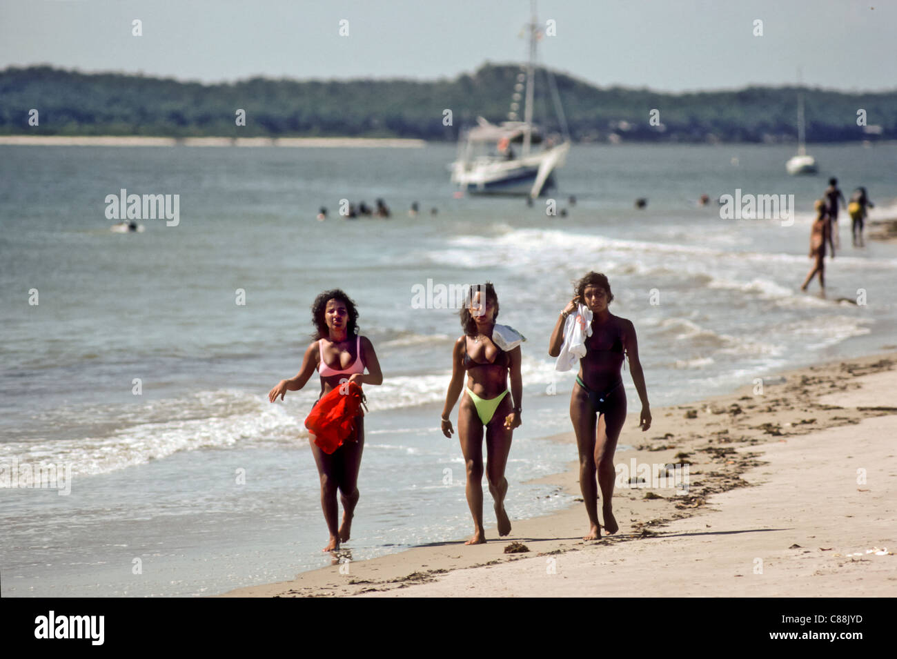 La Isla de Itaparica, Brasil. Tres chicas mulatas caminando en una playa  con un yate detrás. El estado de Bahia Fotografía de stock - Alamy