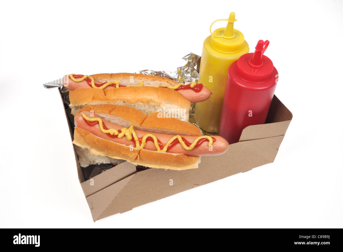 2 perros calientes con rollos en una bandeja para llevar con la mostaza y el ketchup condimentos sobre fondo blanco. Foto de stock