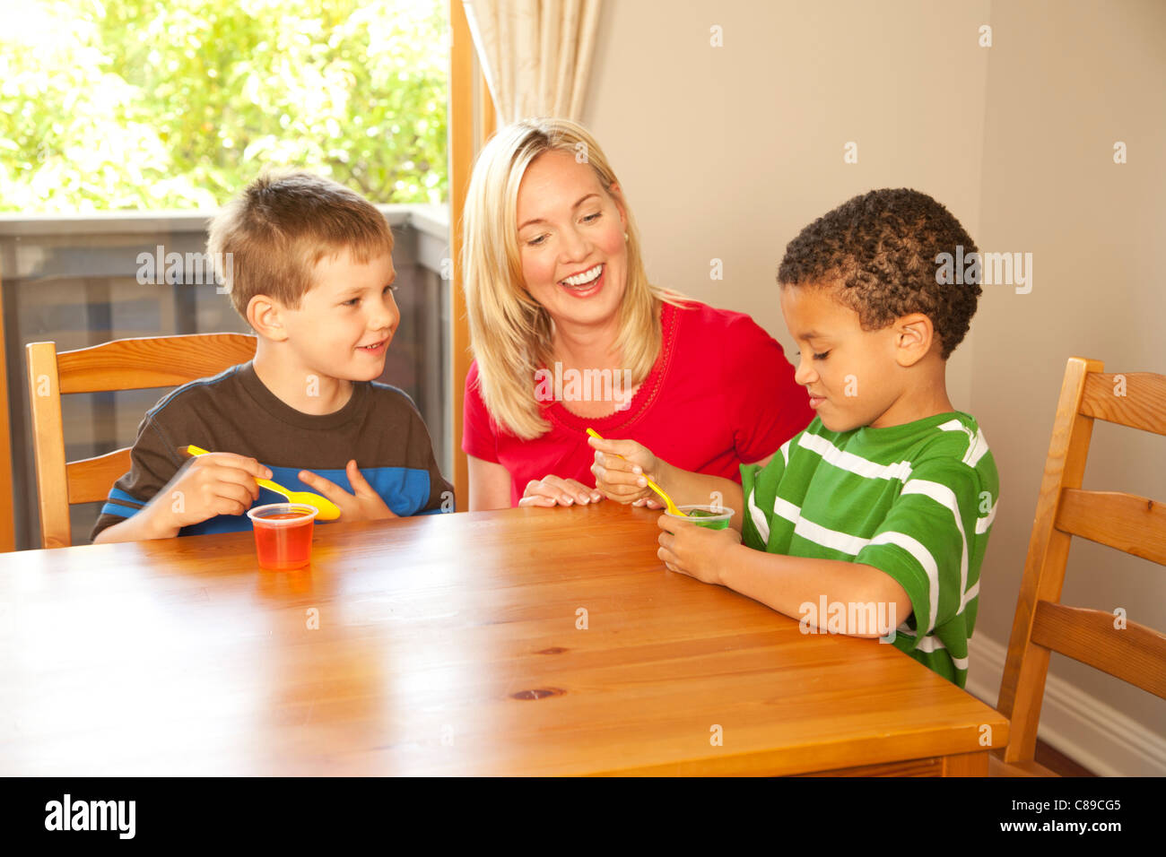 Madre y chicos en una mesa de cocina comiendo Jell-O Foto de stock