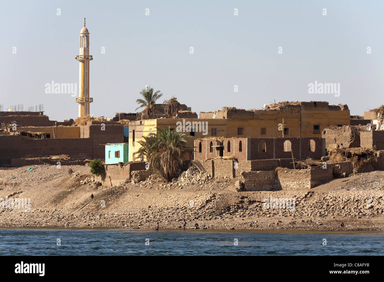 La sección de banco del río Nilo con el tradicional senderismo casas, una en construcción, con restos de barro y un minarete de la mezquita Foto de stock