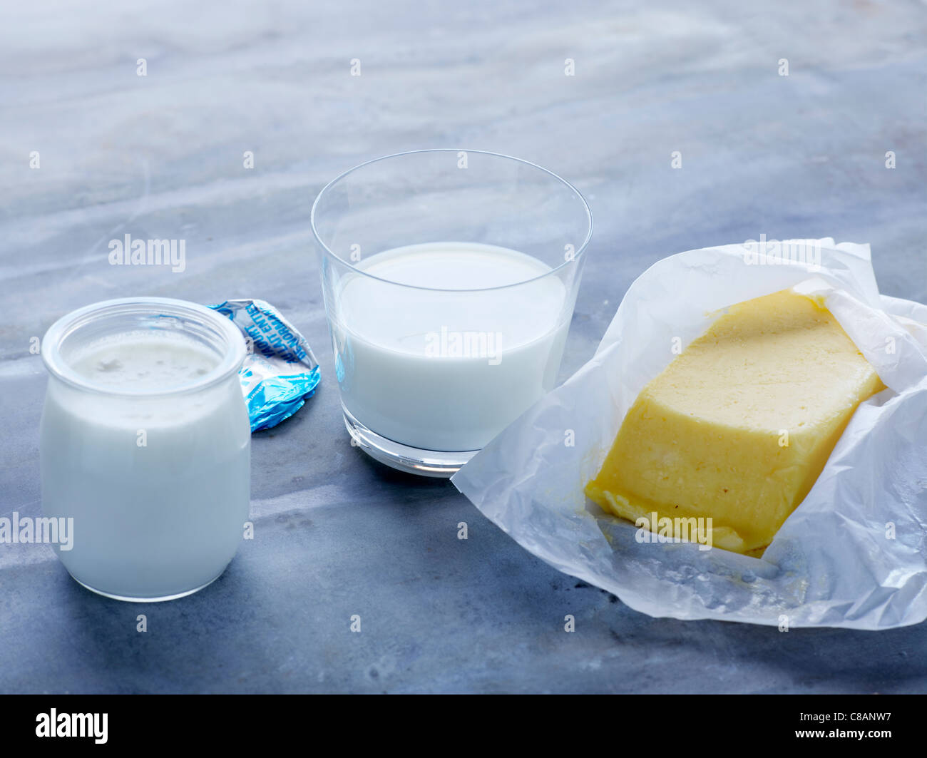 Losa de mantequilla, yogur, y un vaso de leche Foto de stock