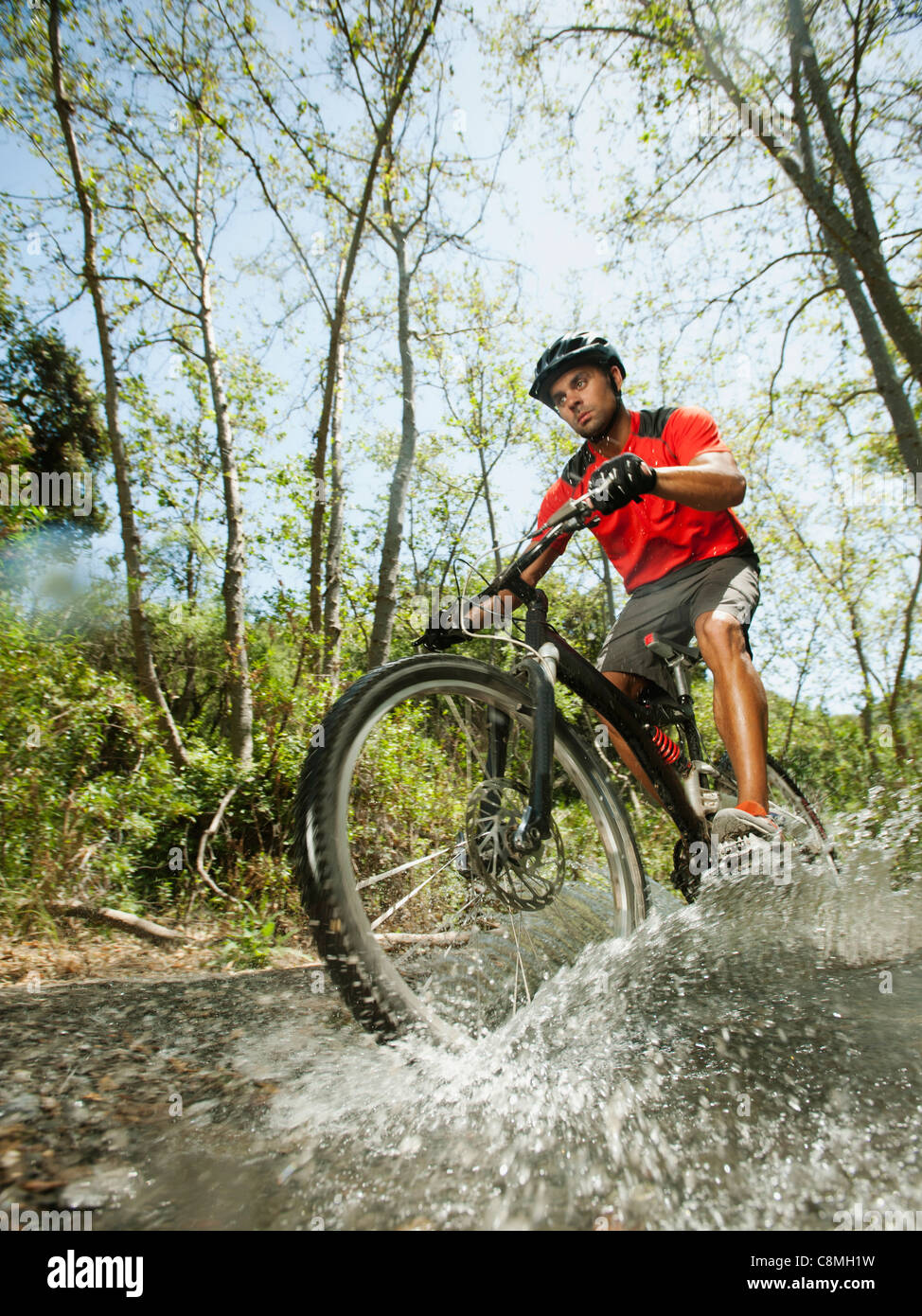 Raza mixta hombre montando en bicicleta de montaña a través de stream Foto de stock