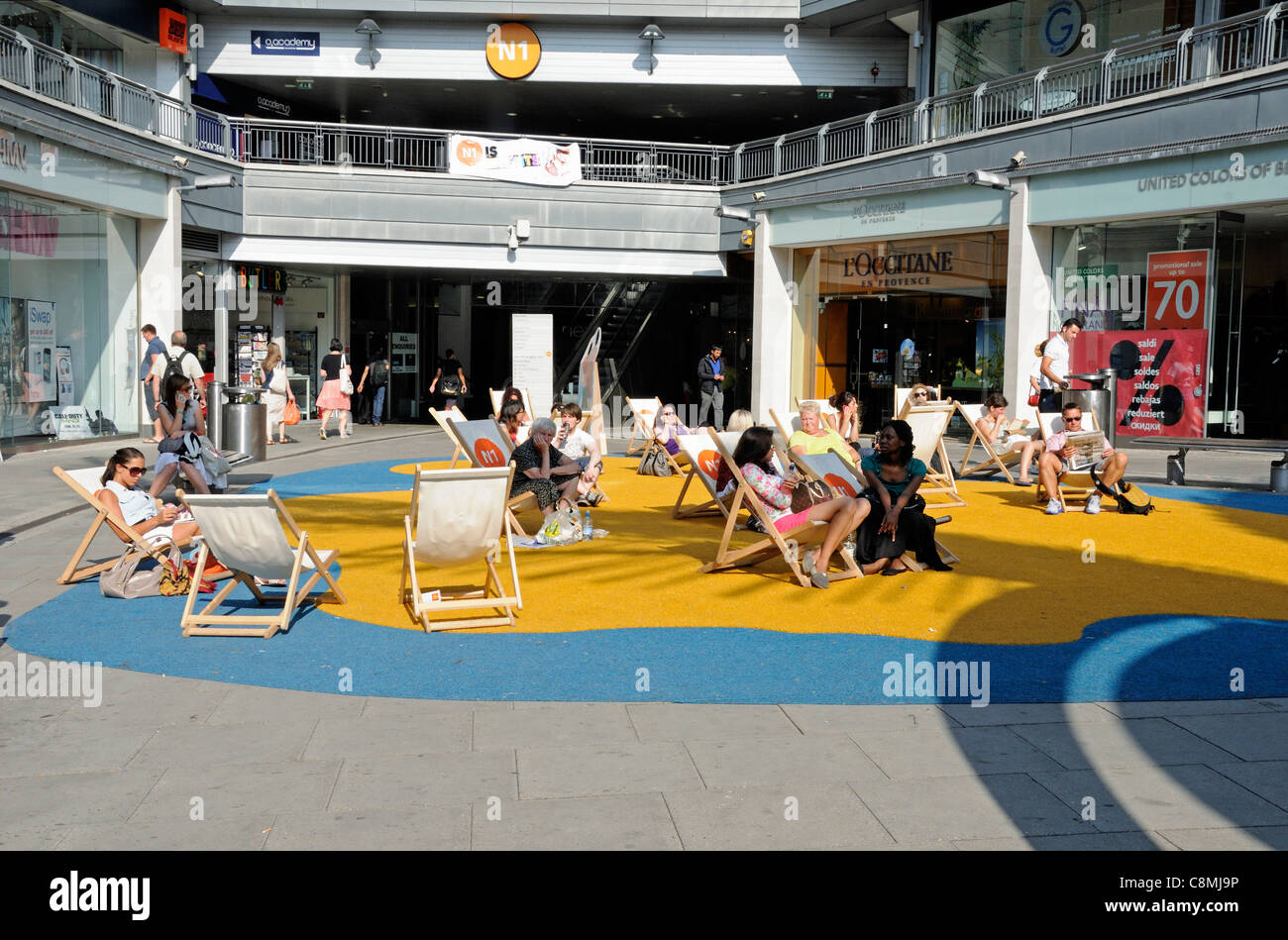 Las personas relajarse en tumbonas en la imitación arena en el centro de N1, Angel Islington, Londres, Inglaterra Foto de stock