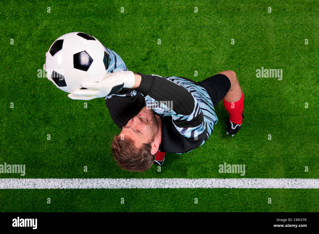 Fotografía aérea de un portero de fútbol saltar en el aire, guardando la pelota en la línea. Punto de enfoque está en su rostro. Foto de stock