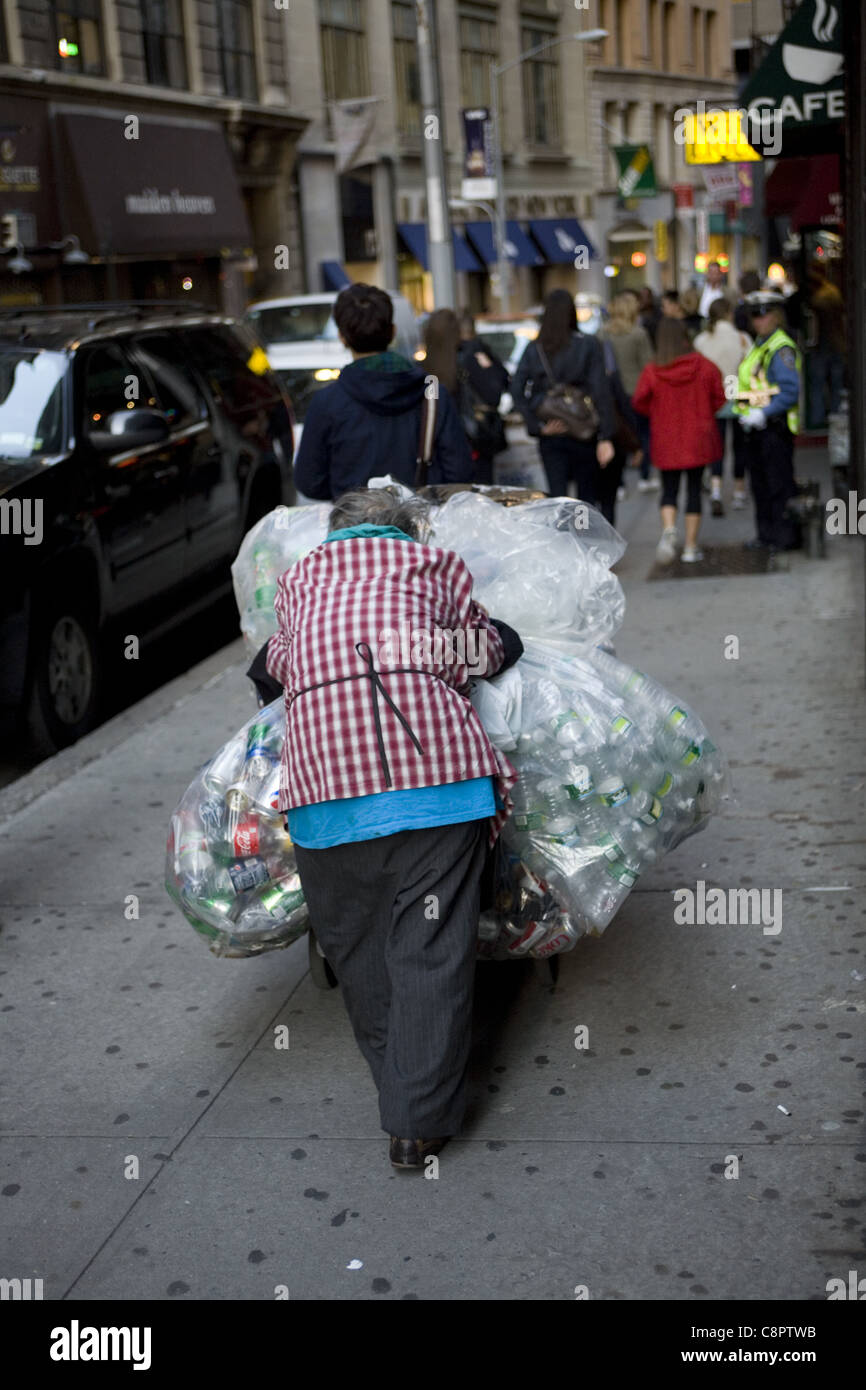 Mujer de edad recogiendo latas de aluminio en la calle en el distrito financiero de Nueva York refleja la economía estadounidense y la creciente pobreza Foto de stock