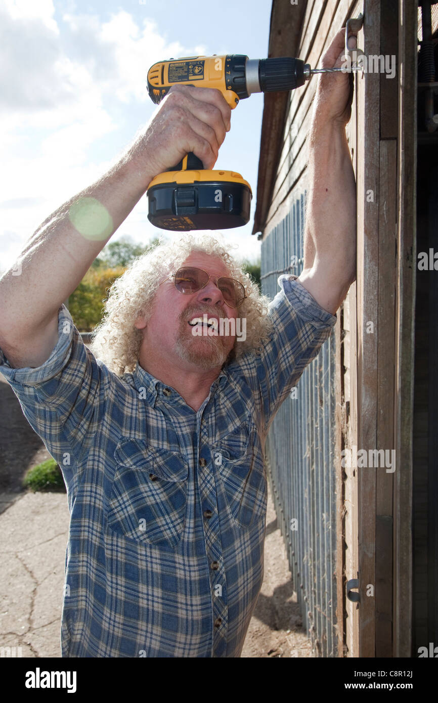 Un hombre usa un taladro inalámbrico para arreglar un broche en un  cobertizo puerta UK Fotografía de stock - Alamy