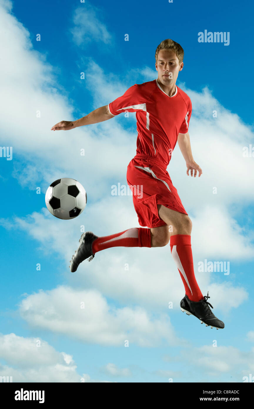 Jugador de fútbol saltando en mitad del aire chutar un balón Foto de stock
