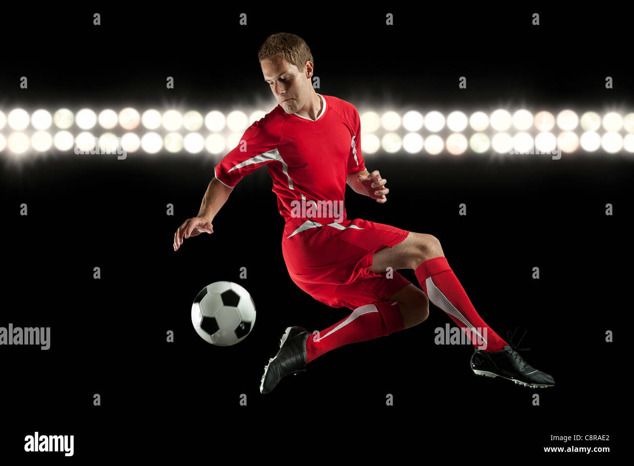 Jugador de fútbol saltando en mitad del aire chutar un balón en la noche Foto de stock
