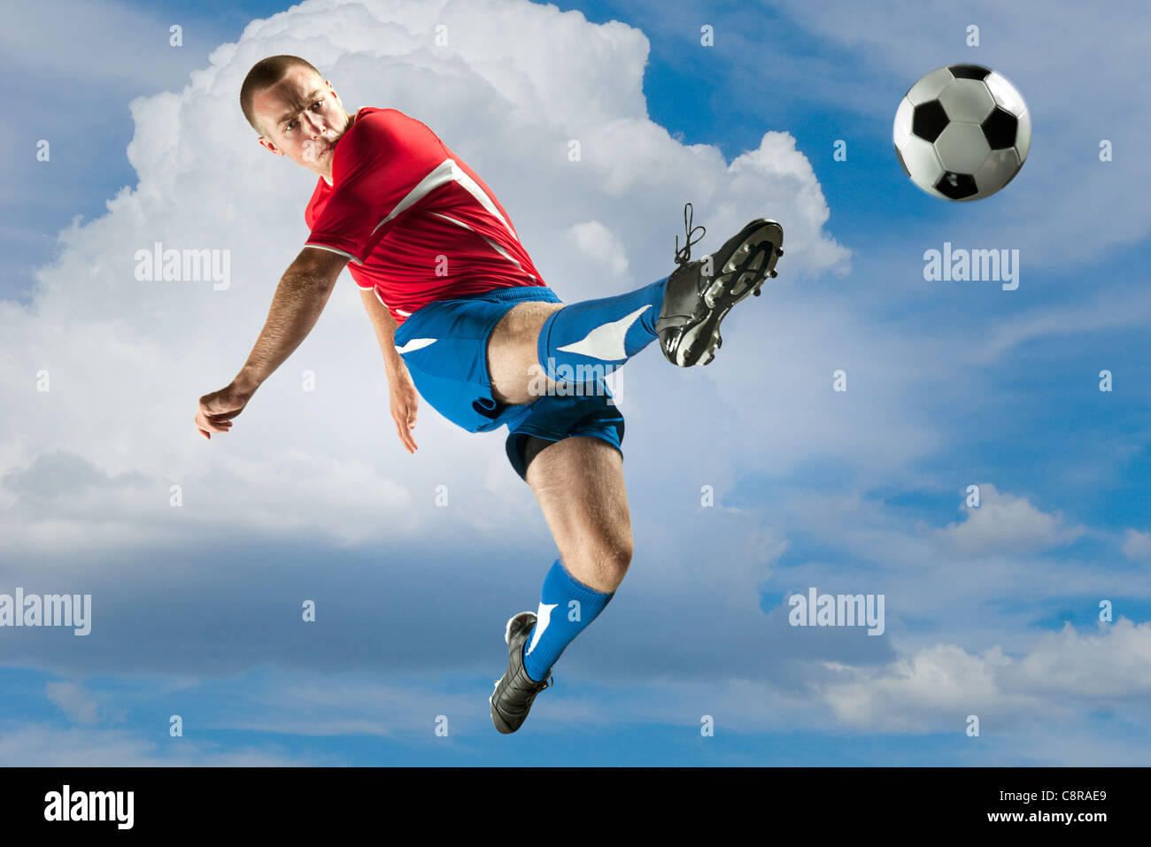 Jugador de fútbol saltando en mitad del aire chutar un balón Foto de stock