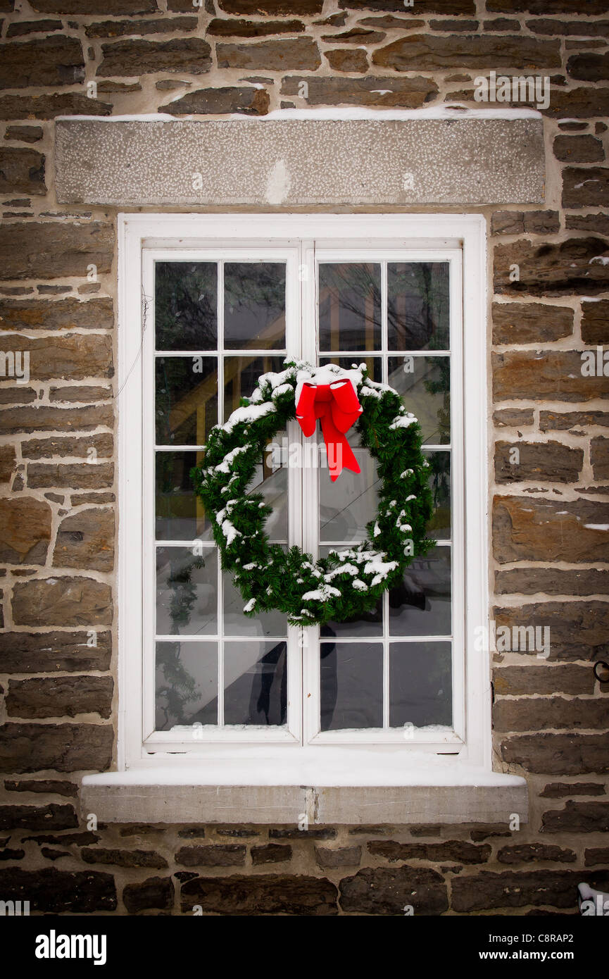 Un verde abeto de Navidad con una cinta roja que cuelga en el centro de una vieja, la nieve cubrió la ventana en muro de piedra. Foto de stock