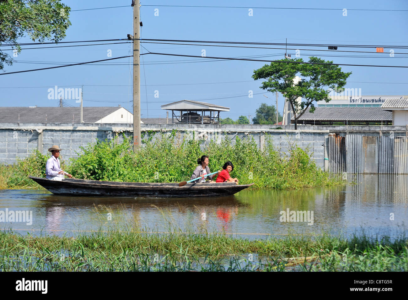 Familia tailandesa pasando una fábrica inundada por bote a remo, Tailandia se vio afectado por graves inundaciones en 2011 Foto de stock