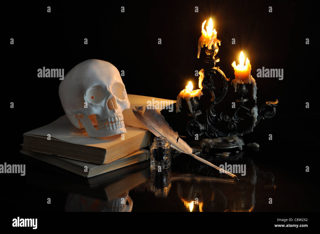 Bodegón con cráneo, libros y velas sobre fondo negro Foto de stock