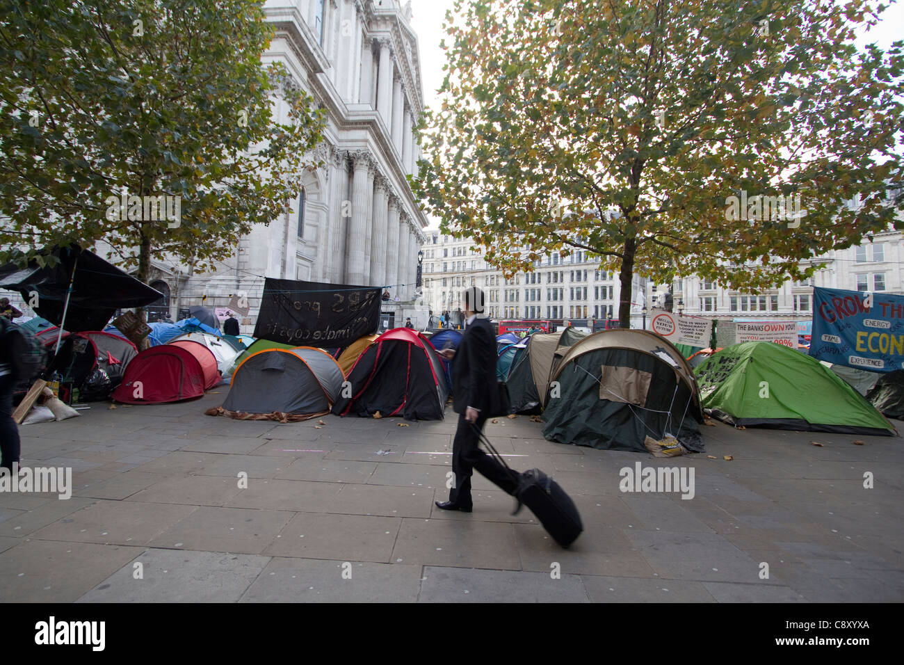 Ocupar Londres manifestantes Saint Pauls St Pauls acampar en la ciudad de carpas con trabajadores de la ciudad caminando pasado Foto de stock