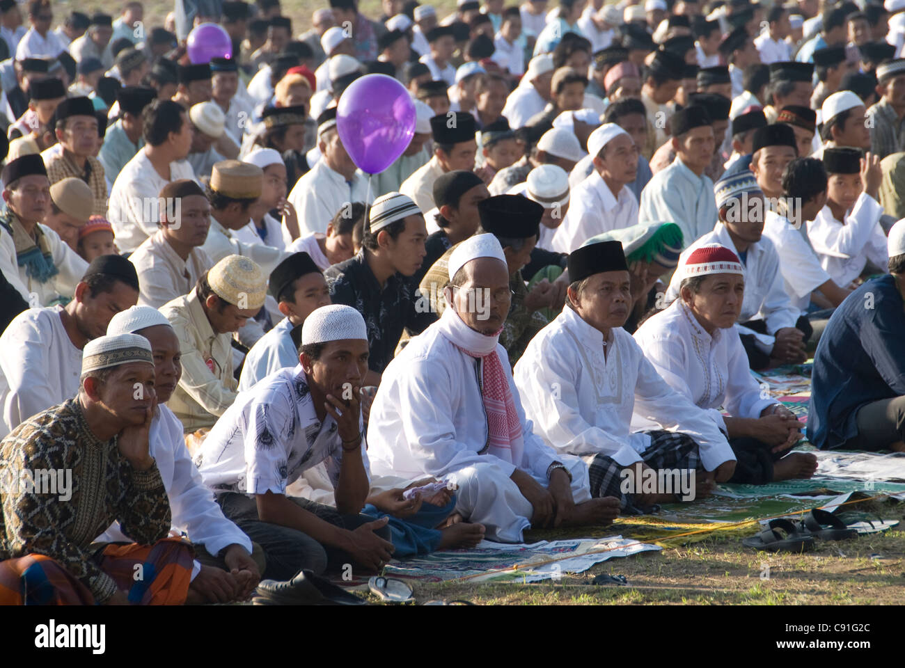 Hombres y niños sentados con patas cruzadas con gorras pegi musulmanas, ceremonia Idul Fitri, Denpasar, Bali, Indonesia, Asia Foto de stock
