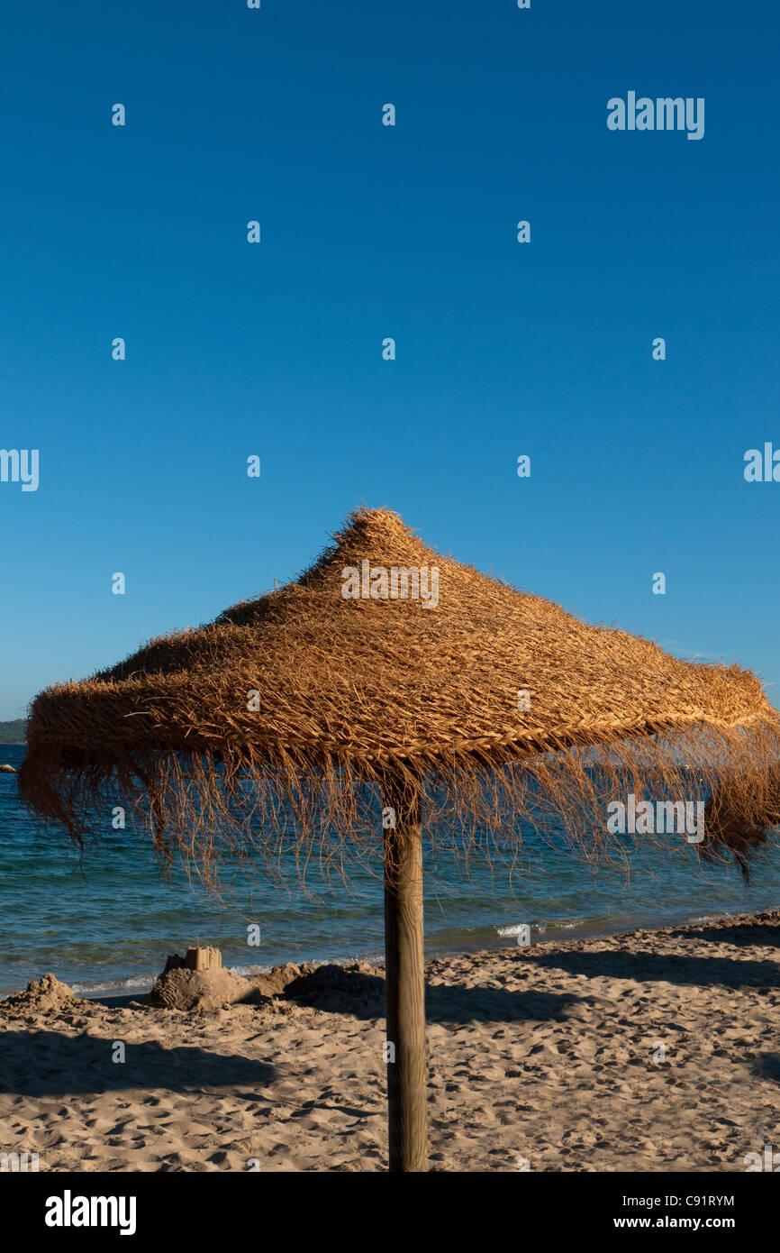 Sombrilla de mimbre en la soleada playa de verano, Puerto de Pollensa, Mallorca, España Foto de stock
