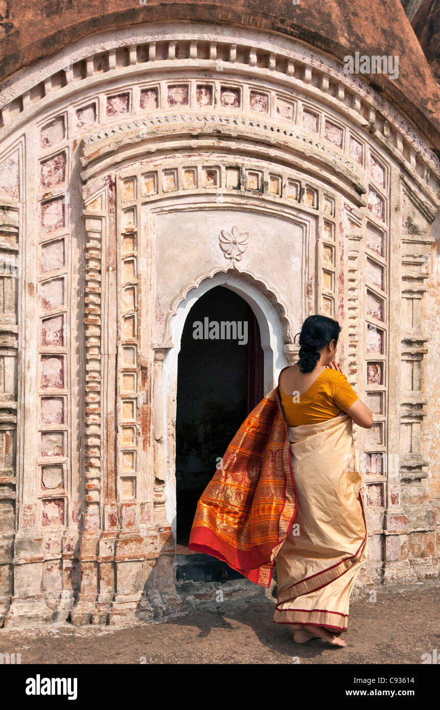 Una mujer hindú luciendo un colorido sari pasa uno de los 108 templos de ladrillo en Kalna Shiva. Foto de stock