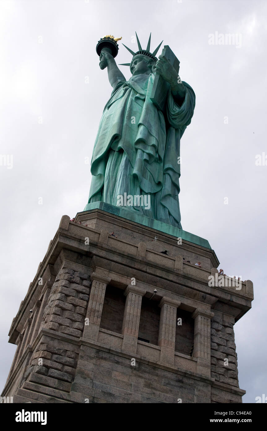 La estatua de la libertad con pequeñas cabezas de gente mirando por encima de la cornisa de pedestal Foto de stock