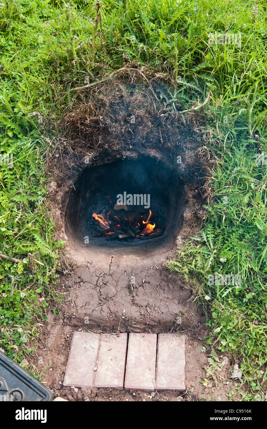 Un horno de tierra o cocinar hoyo cavado en la ladera de un campo. Después  de que el fuego es rastrillar el horno permanece lo suficientemente  caliente para cocinar Fotografía de stock -
