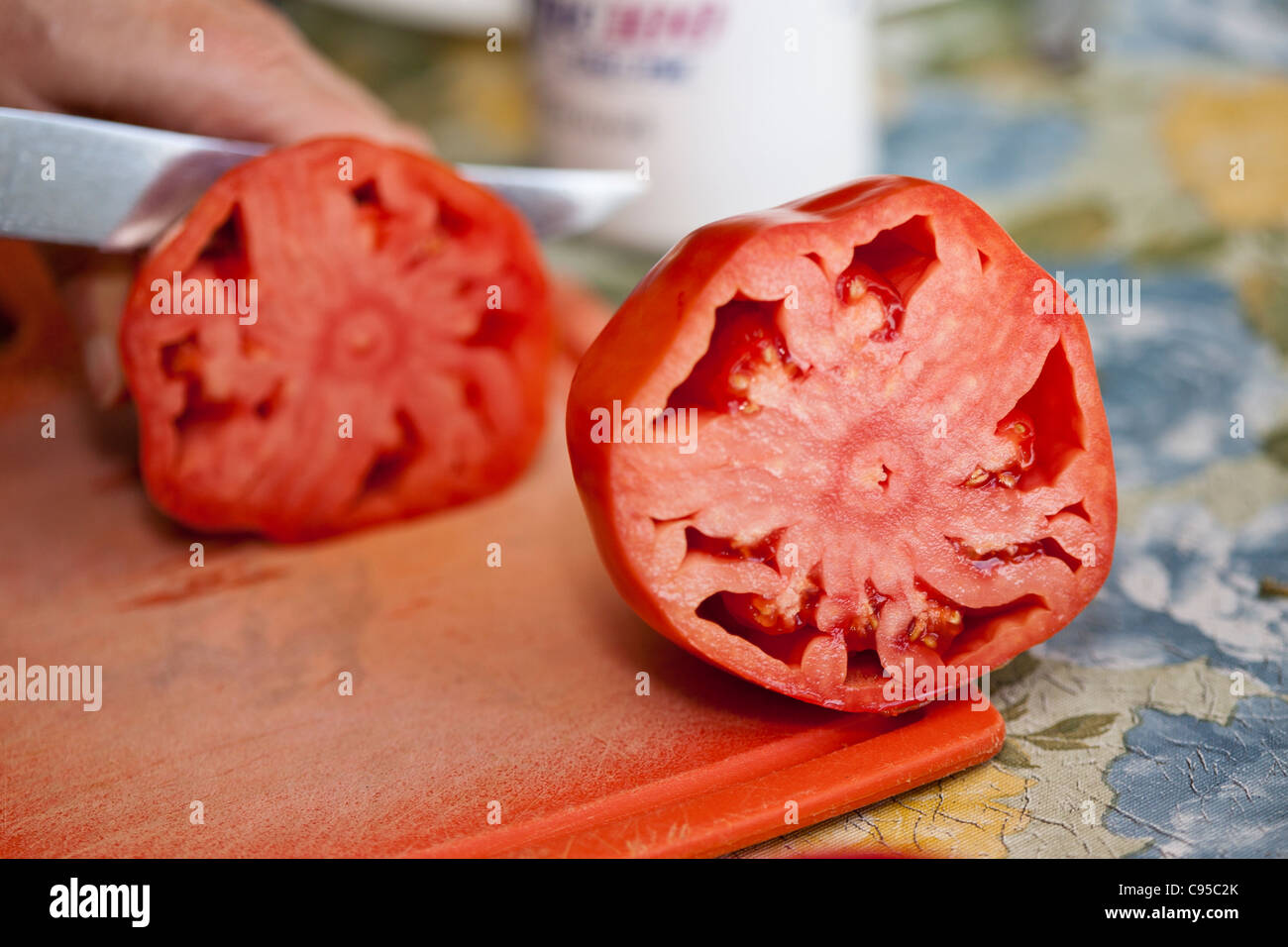 La mitad de un tomate Oxheart carnoso. Una gran muestra de tomate corazón de buey se redujo a la mitad, mientras que la otra mitad está cortada en el fondo Foto de stock