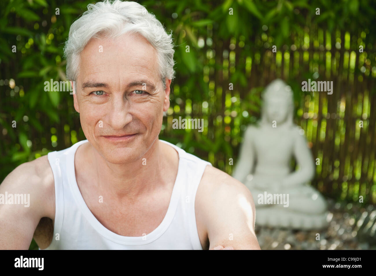Alemania, Baviera, Madura Hombre sonriendo con estatua de Buda en segundo plano. Foto de stock