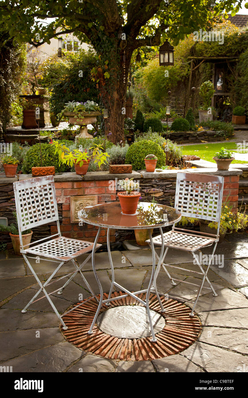 Mesa y sillas de metal sobre piedra patio jardín de otoño en inglés Foto de stock