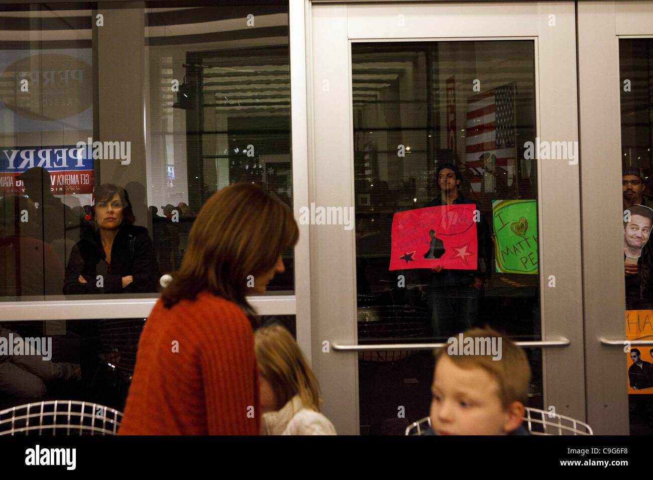 El 20 de diciembre, 2011 - Davenport, Iowa, EE.UU. - Personas sostienen carteles con rostros de Matthew Perry de la ''Amigos'' de televisión - satíricamente alegando pensaron Matthew Perry y Chandler iban a visitar - mientras que el candidato presidencial republicano, el Gobernador de Texas. Rick Perry, habla durante una campaña Foto de stock